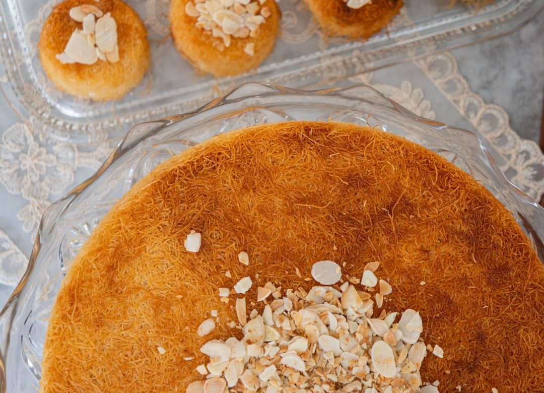 A tray of orange knafeh being cut and served onto paper plates